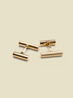 Two gold cufflinks on a light beige background.