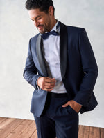 Man in a navy tuxedo with a bow tie, smiling and adjusting his attire.