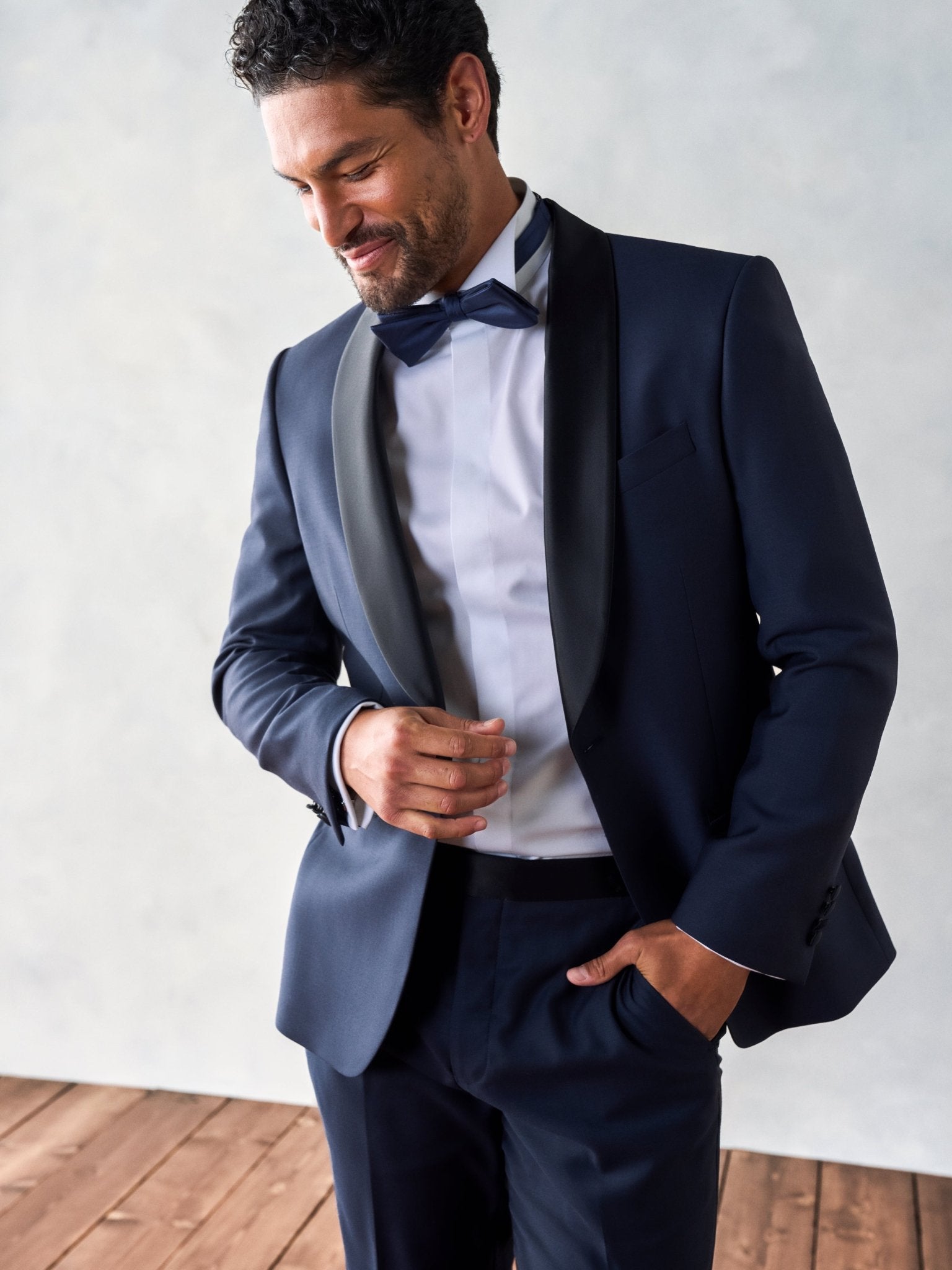 Man in a navy tuxedo with a bow tie, smiling and adjusting his attire.