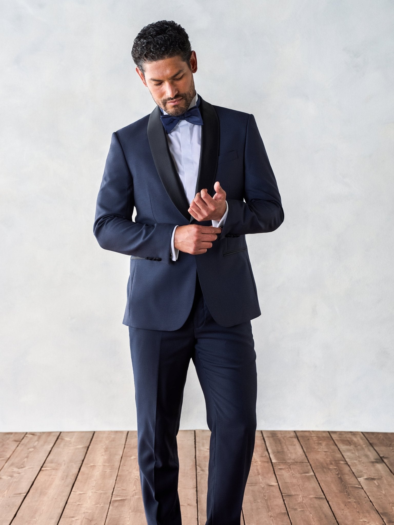 Man adjusting his cufflinks while wearing a navy tuxedo with a bow tie.