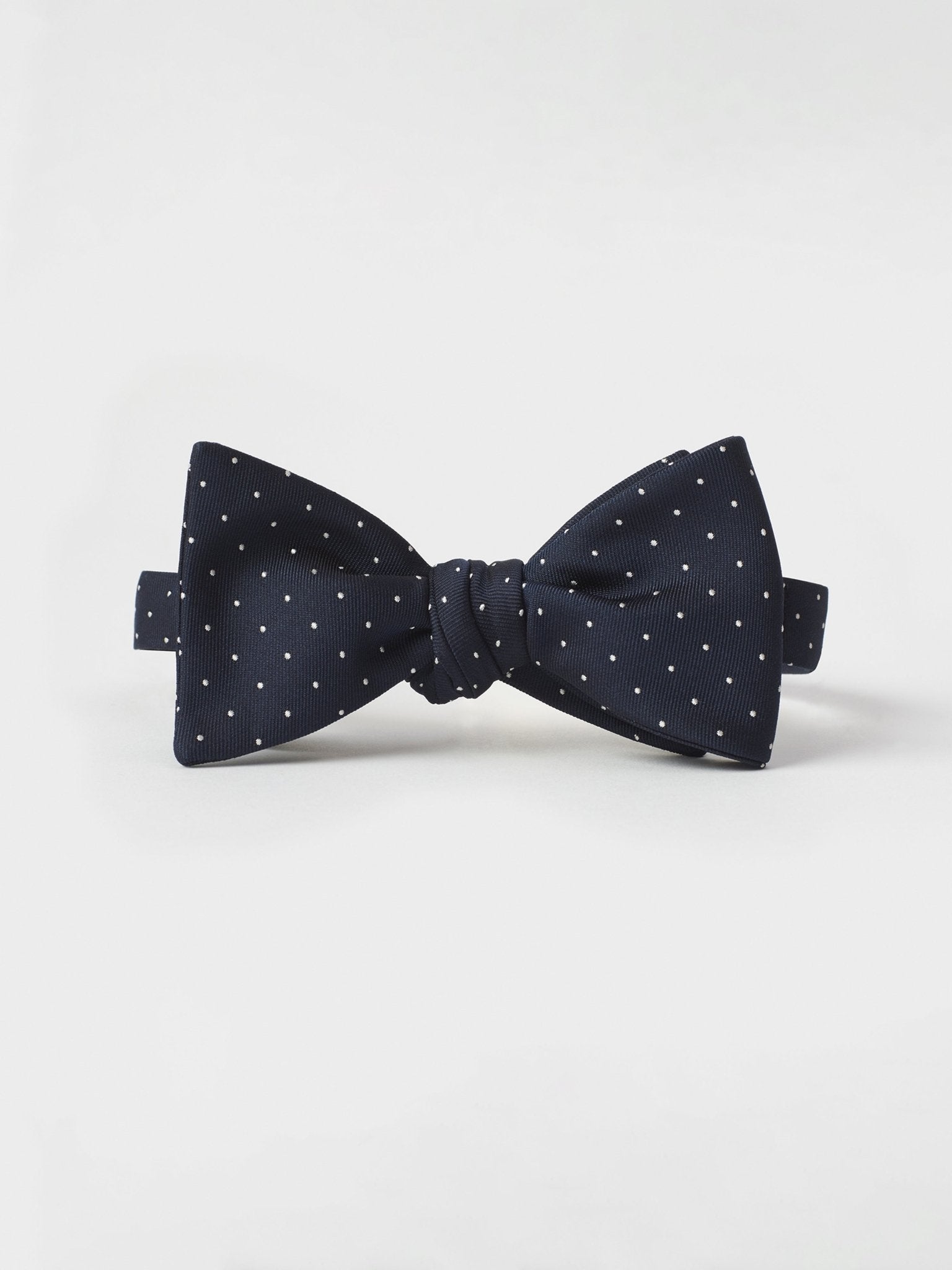 Navy blue bow tie with white polka dots on a plain background.