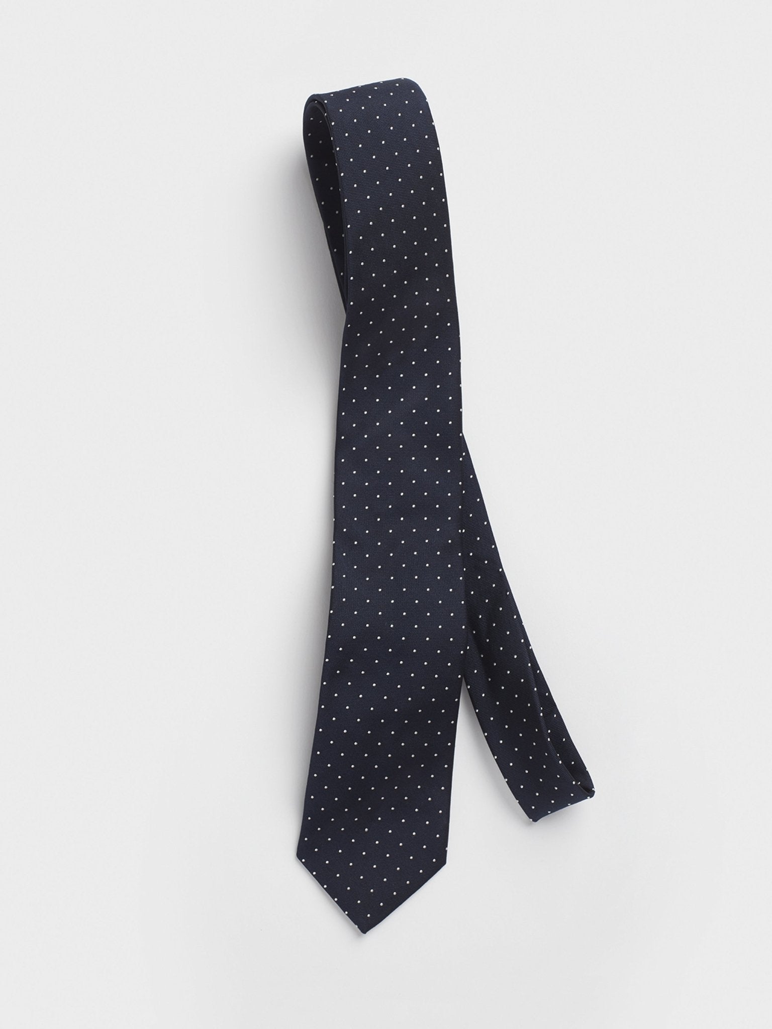 Navy tie with white polka dots hanging against a white background.