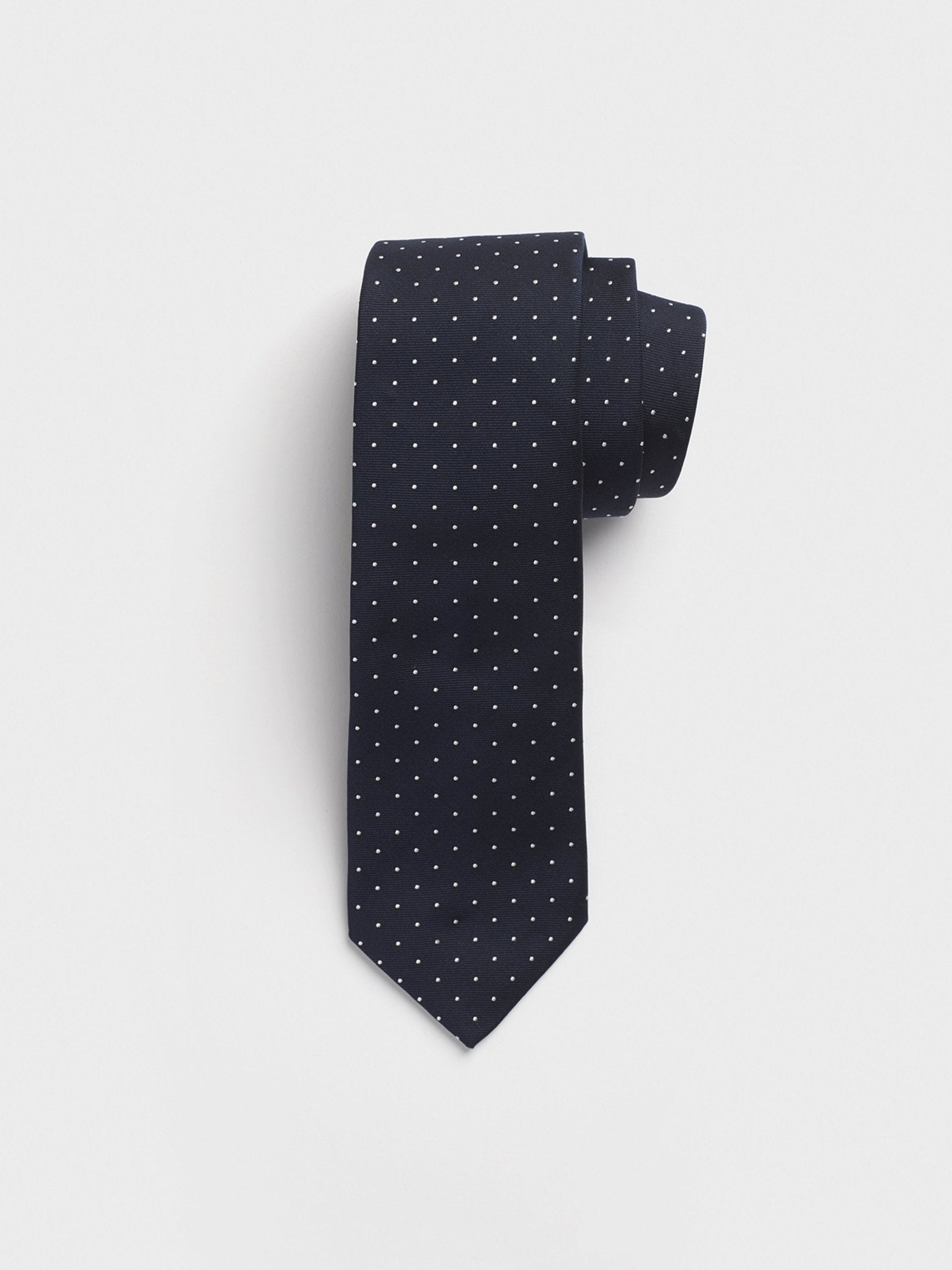 Navy tie with white polka dots, neatly rolled.