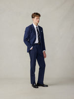 Man wearing a navy suit with a white shirt and striped tie, standing against a neutral background.