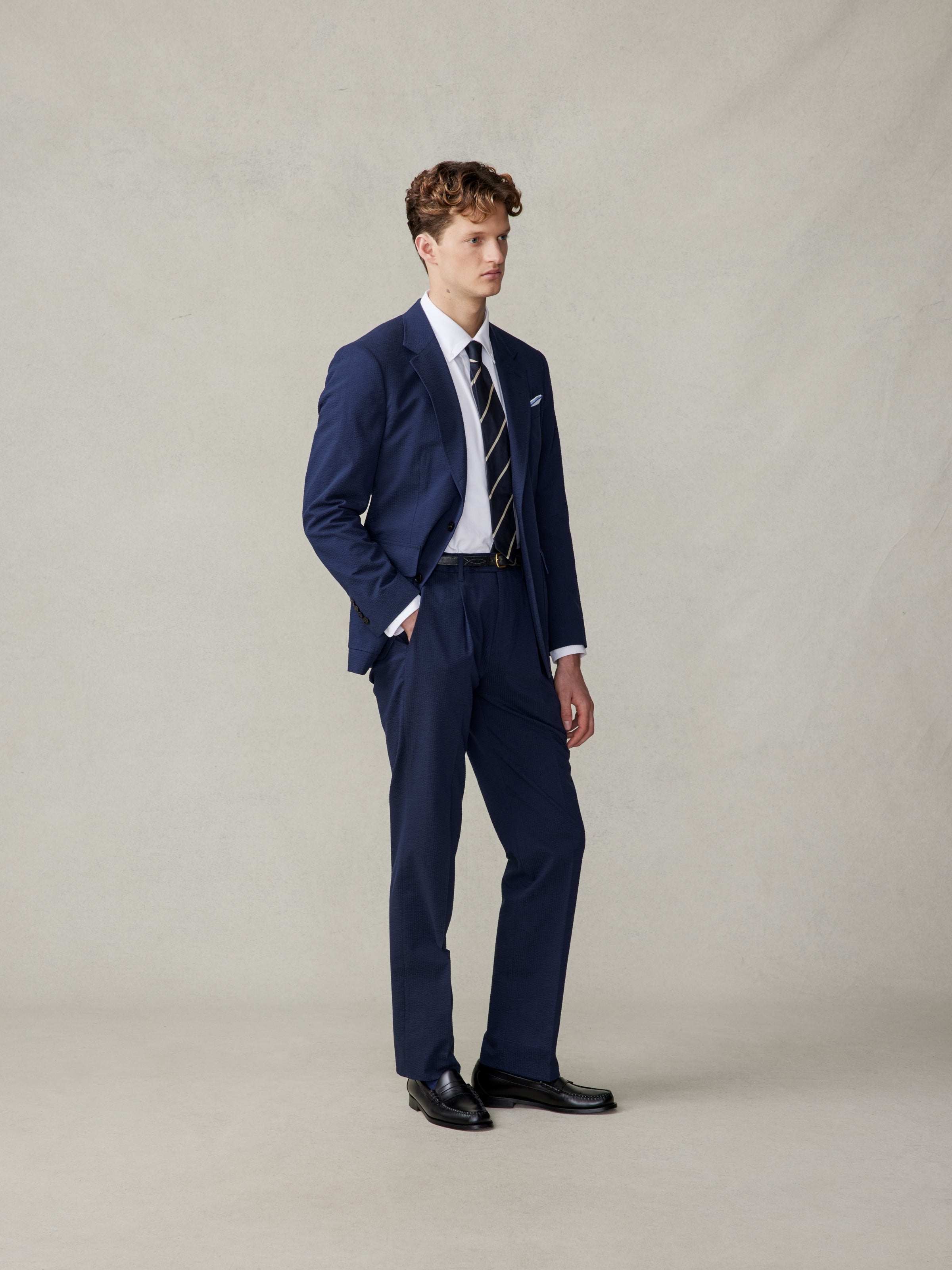 Man wearing a navy suit with a white shirt and striped tie, standing against a neutral background.