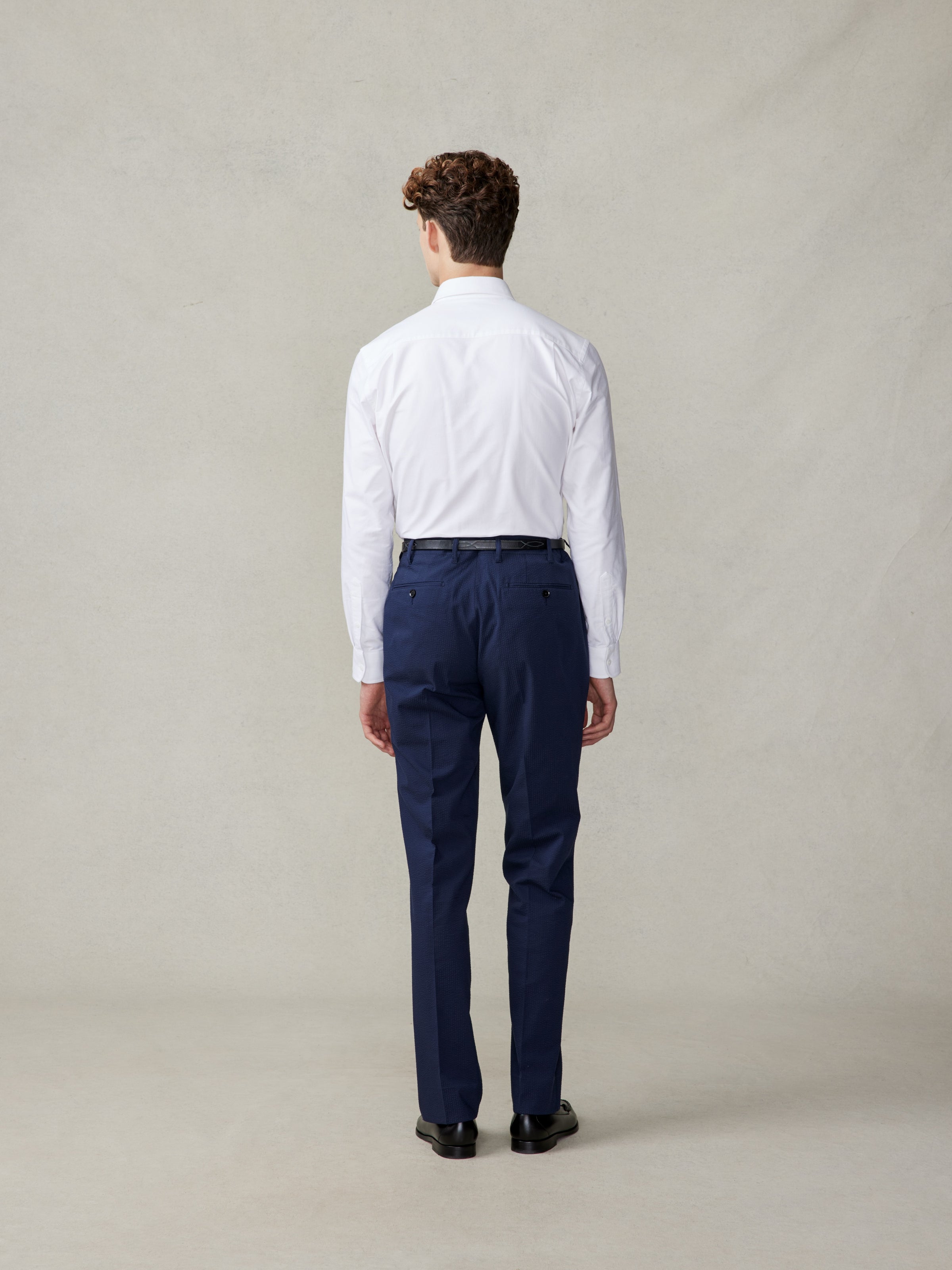 A person wearing a white shirt and navy pants, viewed from the back.