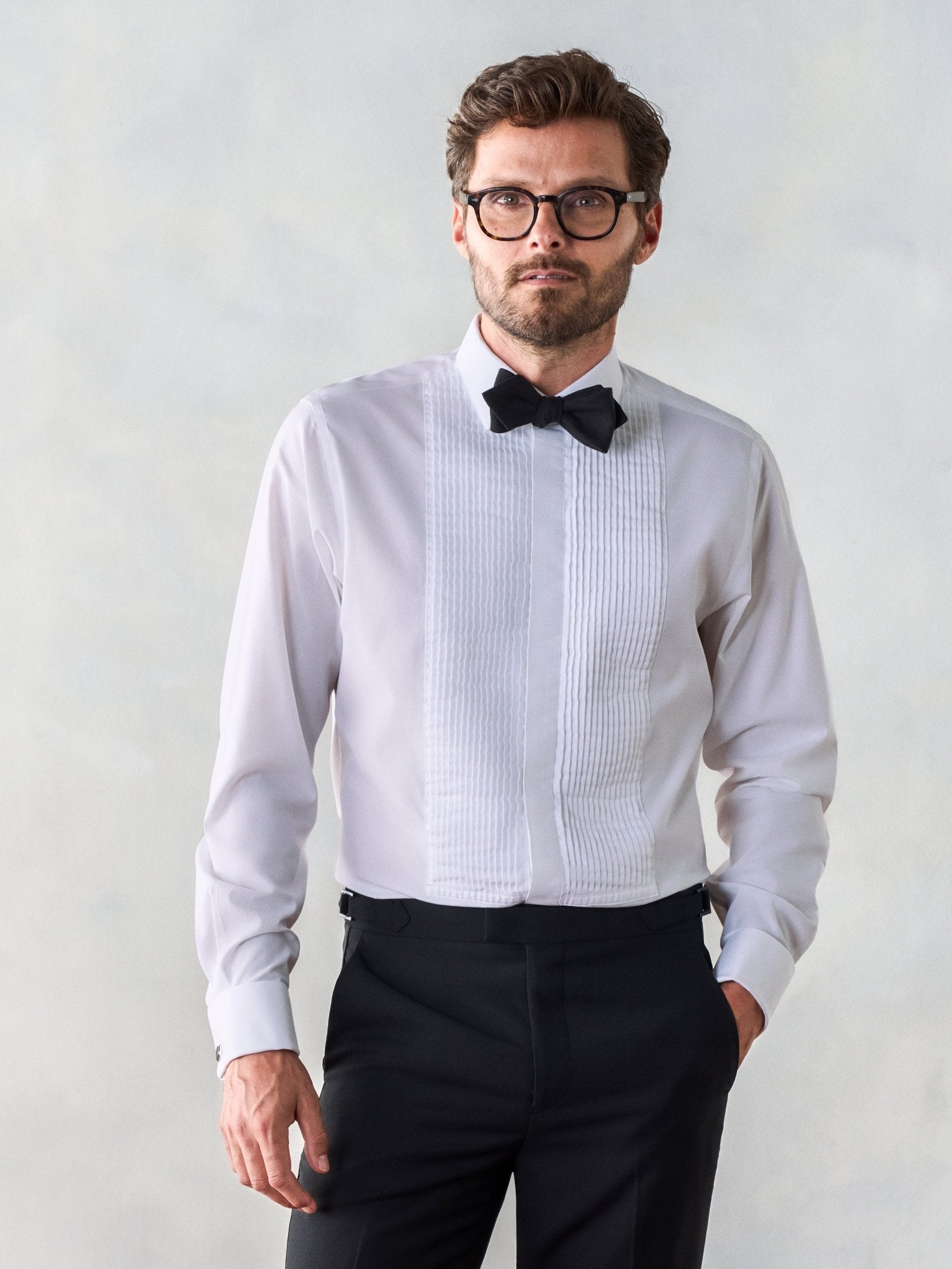 Man wearing a white tuxedo shirt with a black bow tie and black pants.