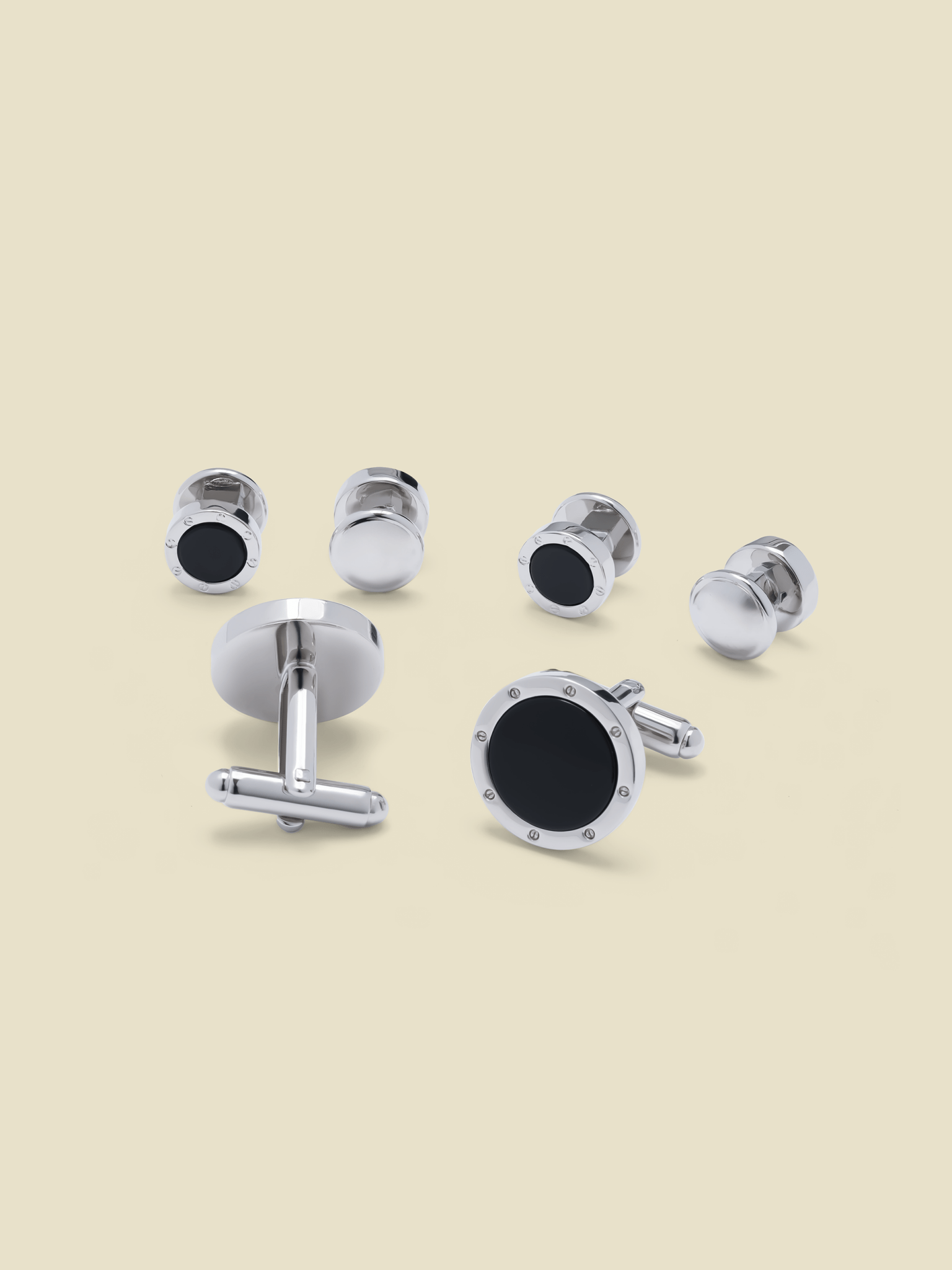 Set of silver cufflinks with black accents on a beige background.