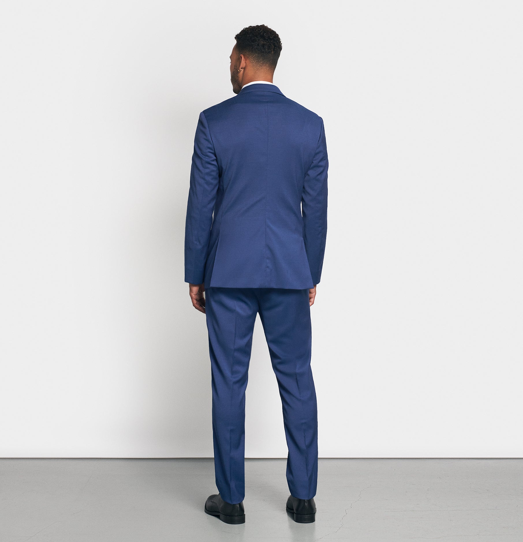 Man wearing a blue suit, viewed from the back, standing on a gray floor.