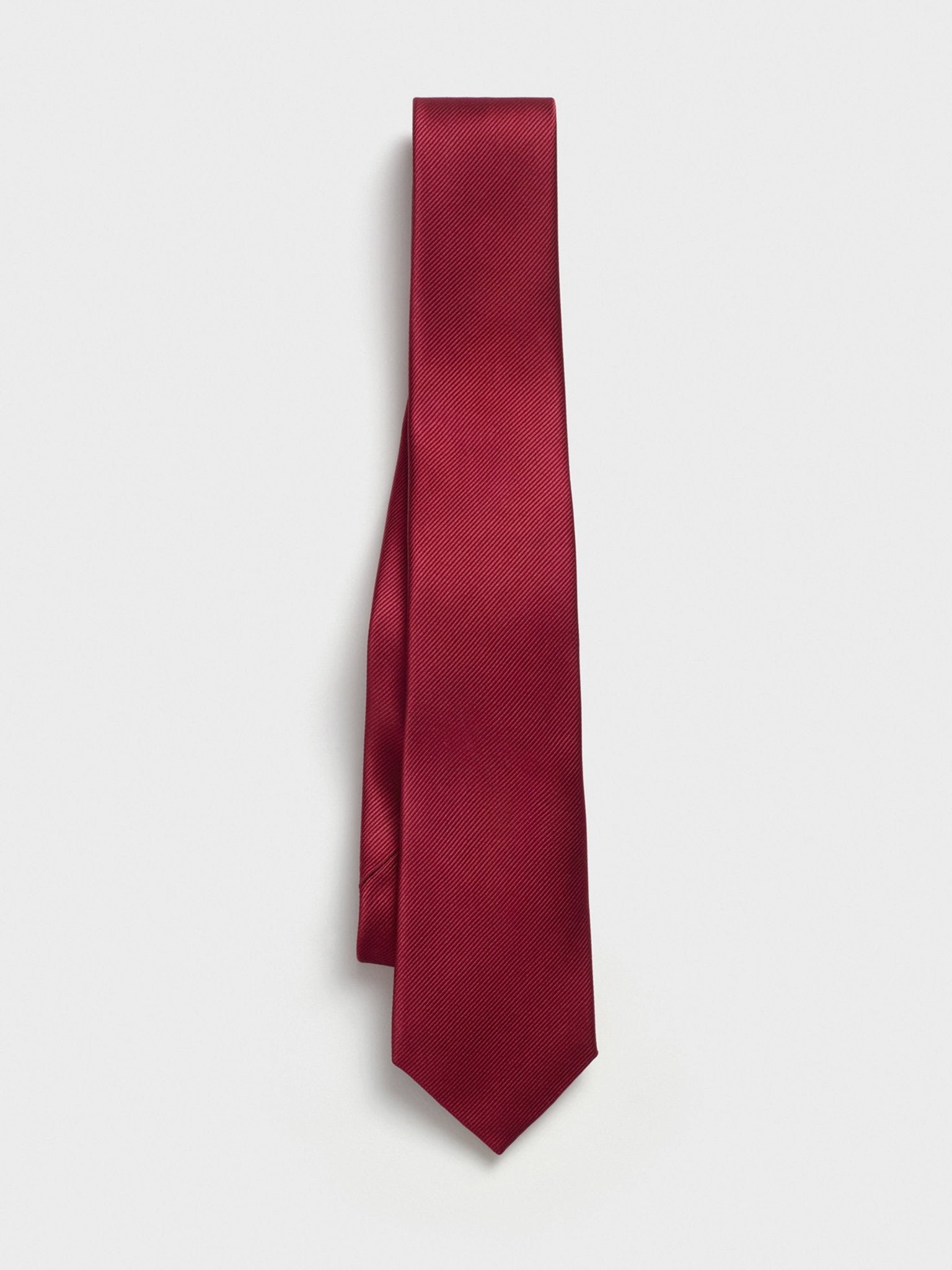 Solid burgundy tie hanging against a white background.
