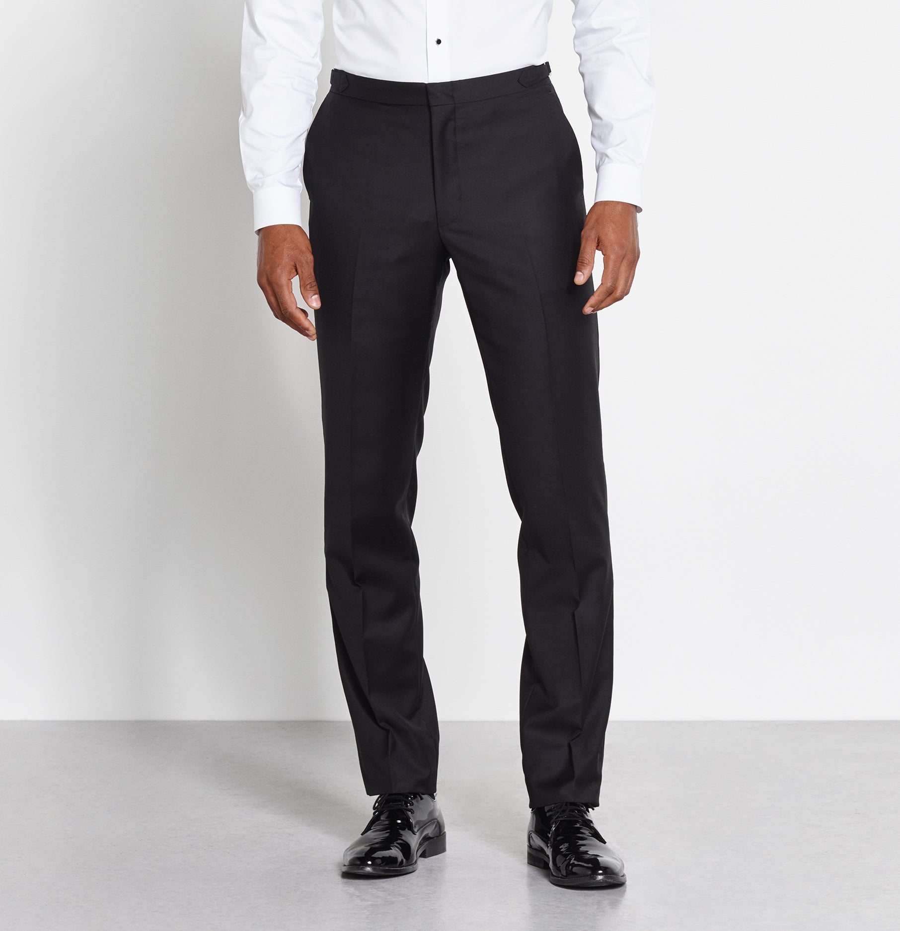 Man wearing black formal trousers and shiny black shoes with a white shirt.