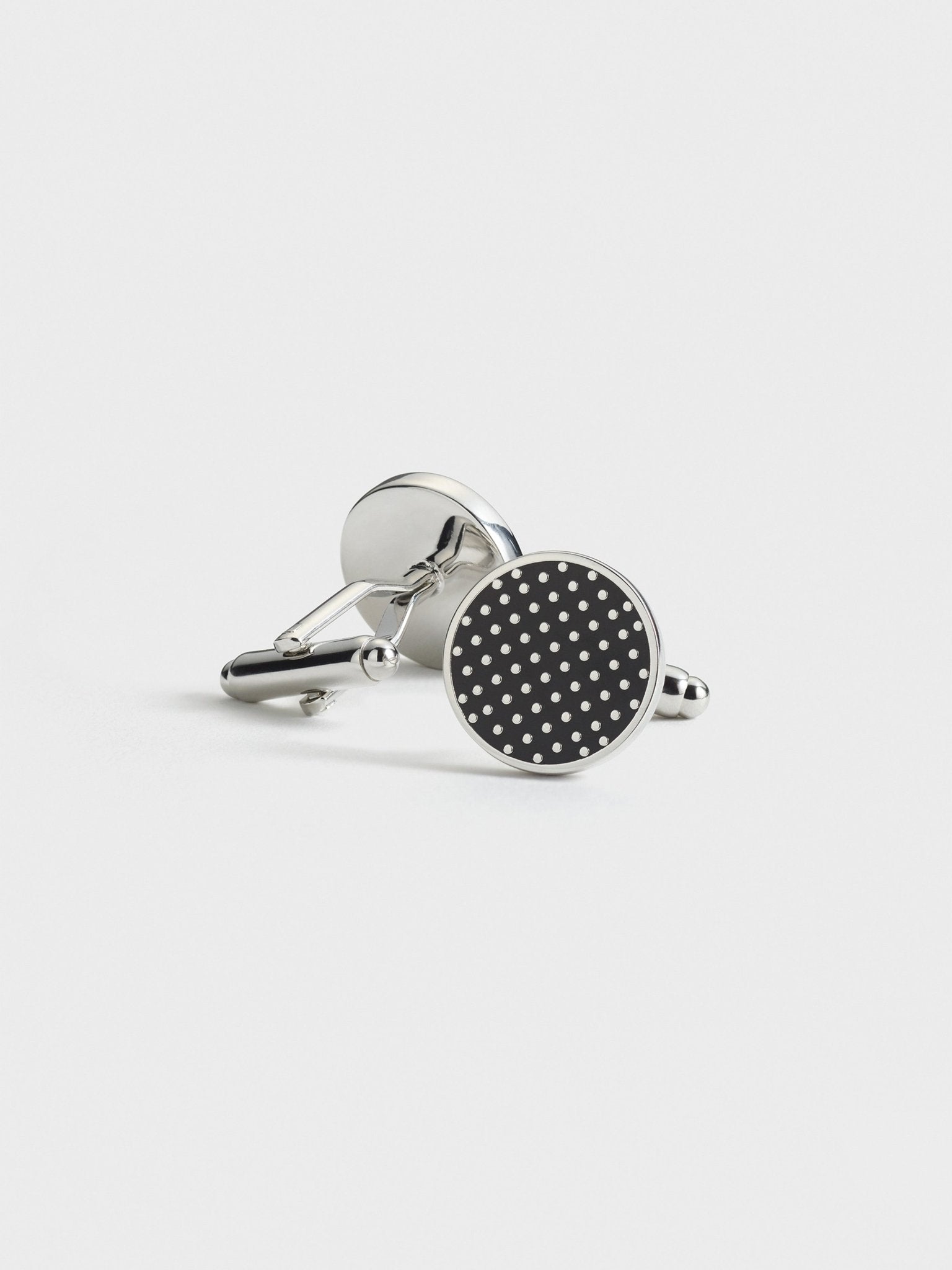 Silver cufflinks with a black circular design and white polka dots.