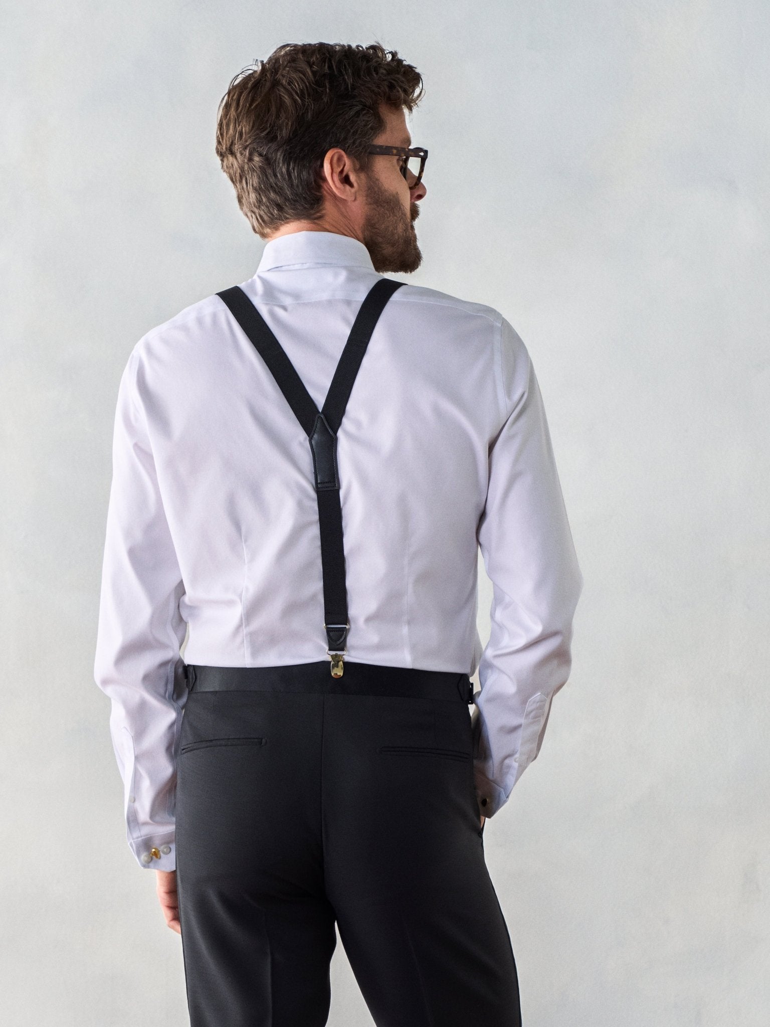 Man wearing a white shirt with black suspenders and black pants, viewed from the back.