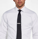 Man wearing a white dress shirt with a black tie and tie clip.