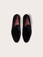 Two black velvet loafers with red insoles on a light background.