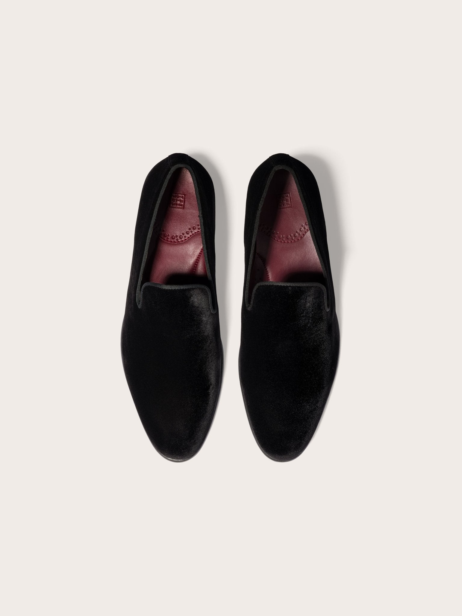 Two black velvet loafers with red insoles on a light background.