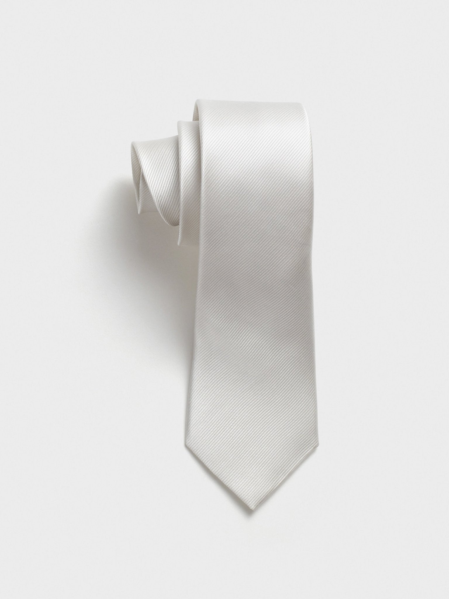 A white tie with a textured pattern, rolled up against a plain background.
